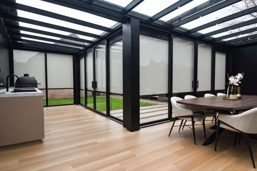 Moderner Wintergarten mit Glasschiebewänden, Outdoor-Küche und schwarzer Aluminiumkonstruktion für stilvolle Outdoor-Living-Bereiche.