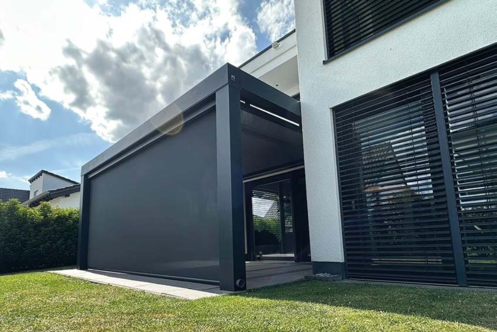 Modernes Pergola-System mit seitlichem Sonnenschutz und schwarzer Aluminiumkonstruktion im Außenbereich eines modernen Wohnhauses.