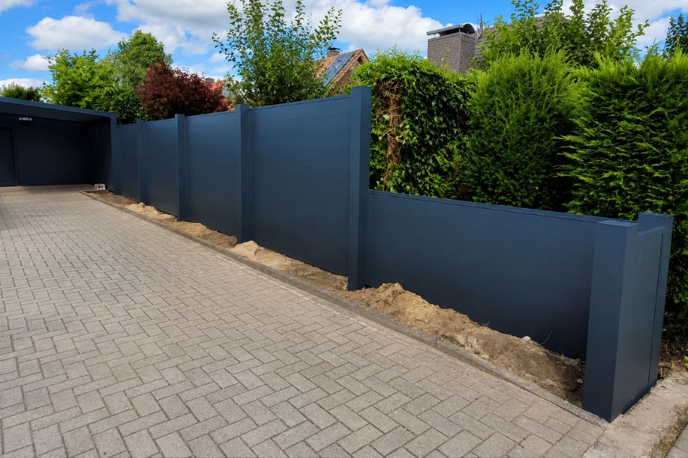 Moderner Sichtschutzzaun mit dunkler Aluminiumoptik und hochwertig gepflasterter Einfahrt im Außenbereich eines Einfamilienhauses.
