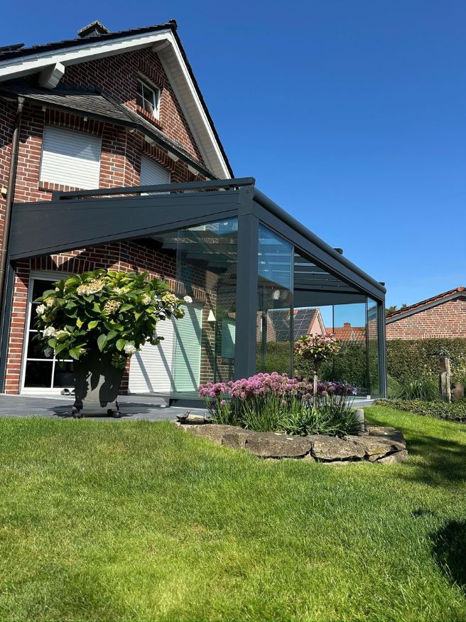 Moderner Wintergarten mit Glasschiebetüren und schwarzer Aluminiumkonstruktion in einem gepflegten Gartenbereich.