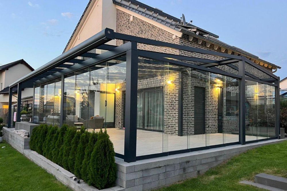Großer Sommergarten mit anthrazitfarbener Aluminiumkonstruktion, umlaufenden Glas-Schiebewänden und moderner Beleuchtung an einem Einfamilienhaus.